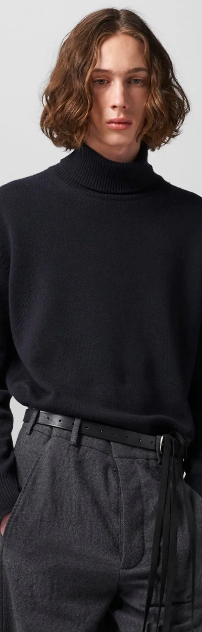 A man wearing a black Ann Demeulemeester turtleneck with a belt and dark grey dress pants