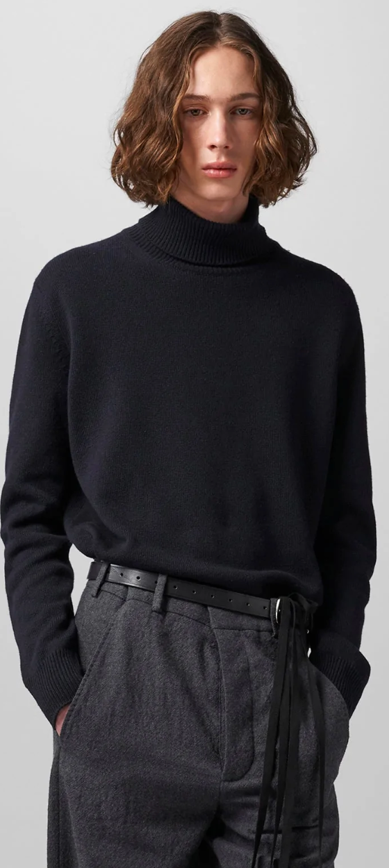 A man wearing a black Ann Demeulemeester turtleneck with a belt and dark grey dress pants