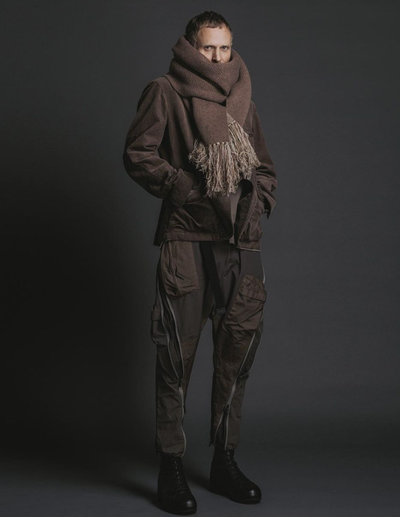 A man wearing The Viridi-Anne oversize brown scarf, a brown jacket with technical looking pants and black hi-top sneakers