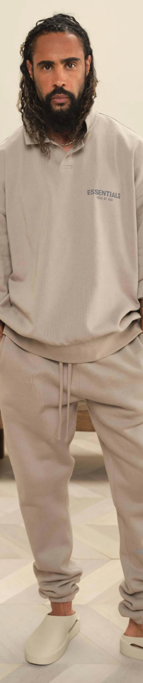 A man wearing Fear of God Essentials loungewear including a beige long-sleeve, matching sweatpants and cream slippers