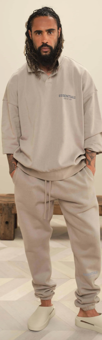 A man wearing Fear of God Essentials loungewear including a beige long-sleeve, matching sweatpants and cream slippers