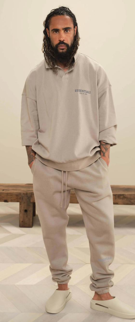 A man wearing Fear of God Essentials loungewear including a beige long-sleeve, matching sweatpants and cream slippers