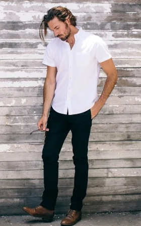 A man wearing a Buck Mason white button-up short-sleeve with black pants and brown loafers