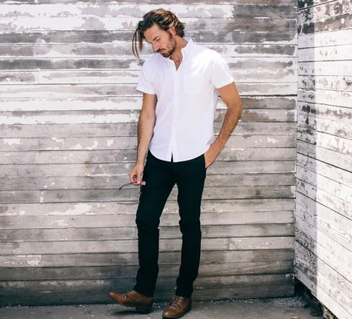 A man wearing a Buck Mason white button-up short-sleeve with black pants and brown loafers