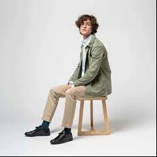 A man sitting and wearing an ISTO green jacket, beige pants and black shoes