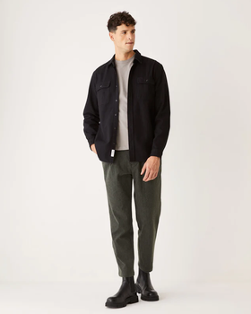 A man wearing a black Frank & Oak button up shirt with dark green pants and black boots