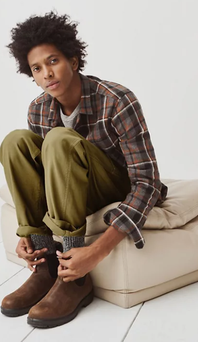 A man sitting and wearing a Madewell plaid button up, green pants and brown blundstone boots