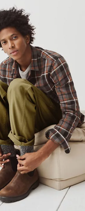 A man sitting and wearing a Madewell plaid button up, green pants and brown blundstone boots