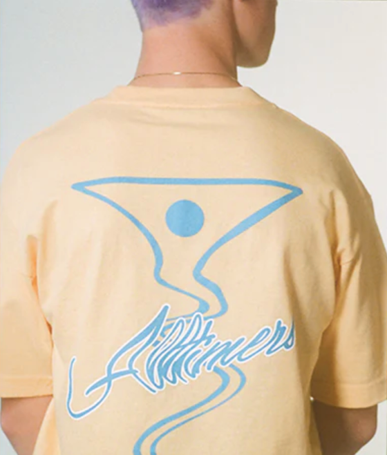 A man wearing a peach and light blue All-timers t-shirt with a martini graphic on it