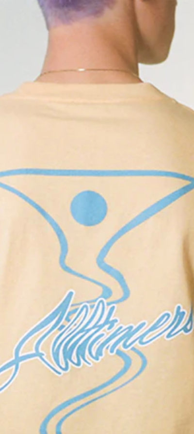 A man wearing a peach and light blue All-timers t-shirt with a martini graphic on it