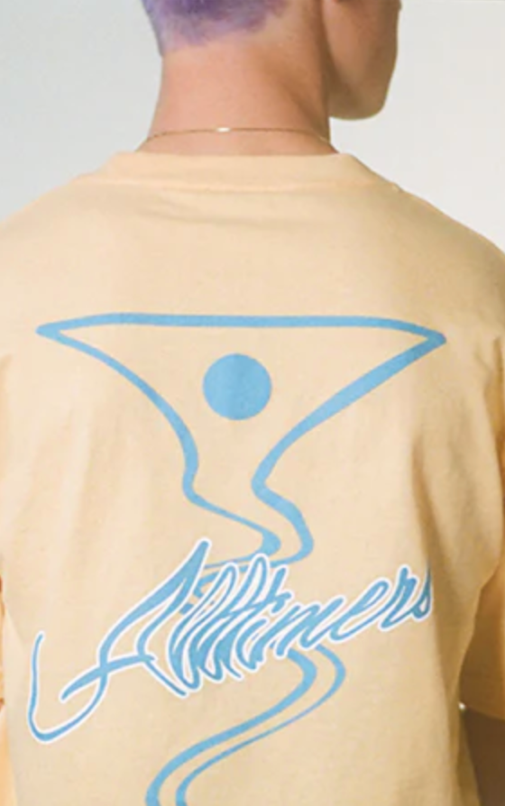 A man wearing a peach and light blue All-timers t-shirt with a martini graphic on it