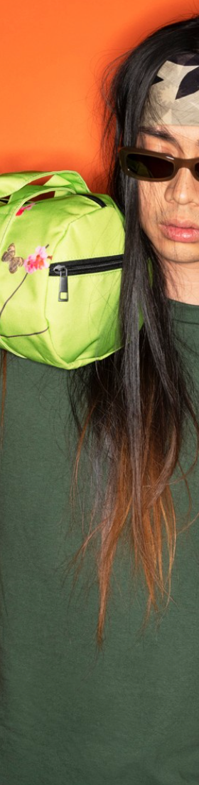 A man with long hair wearing a green Anti Social Social Club t-shirt while holding a lime green small duffle bag