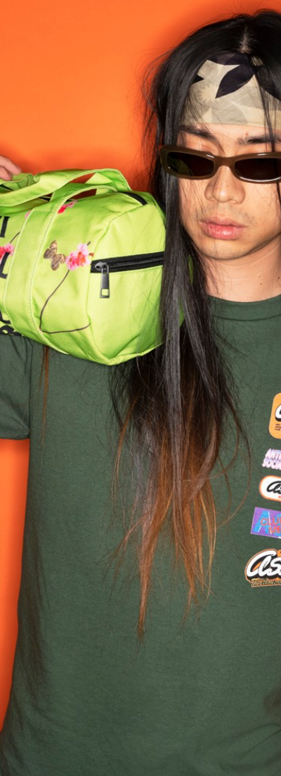 A man with long hair wearing a green Anti Social Social Club t-shirt while holding a lime green small duffle bag