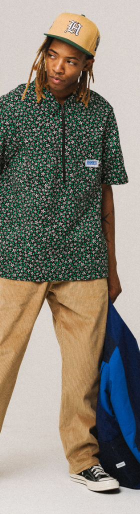A man wearing a green floral The Hundreds short-sleeve button-up, khaki pants and a beige hat