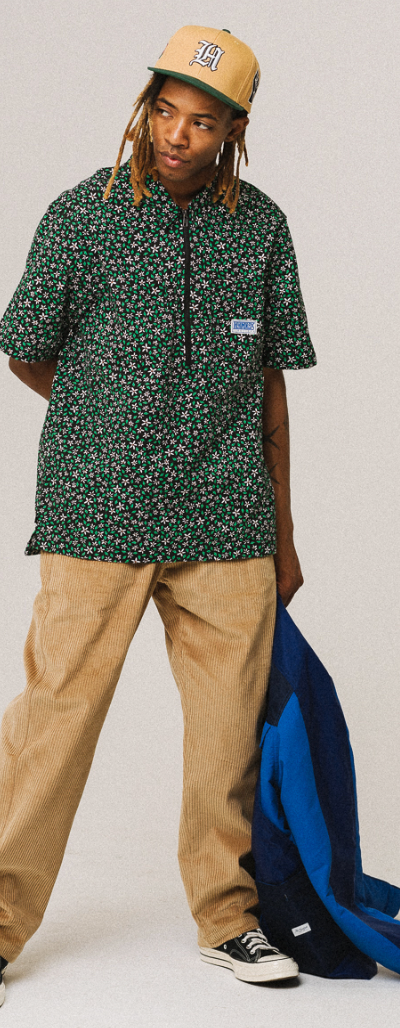 A man wearing a green floral The Hundreds short-sleeve button-up, khaki pants and a beige hat