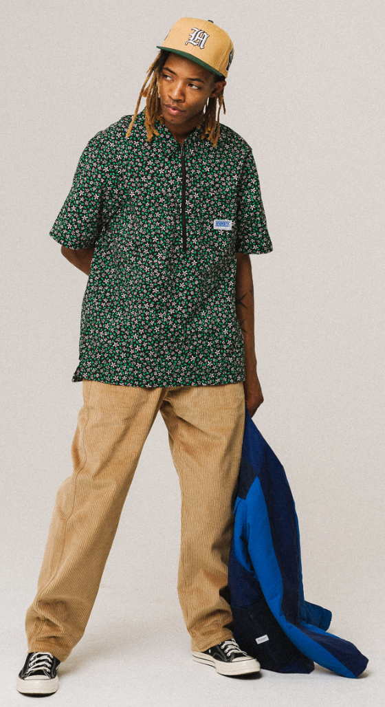 A man wearing a green floral The Hundreds short-sleeve button-up, khaki pants and a beige hat