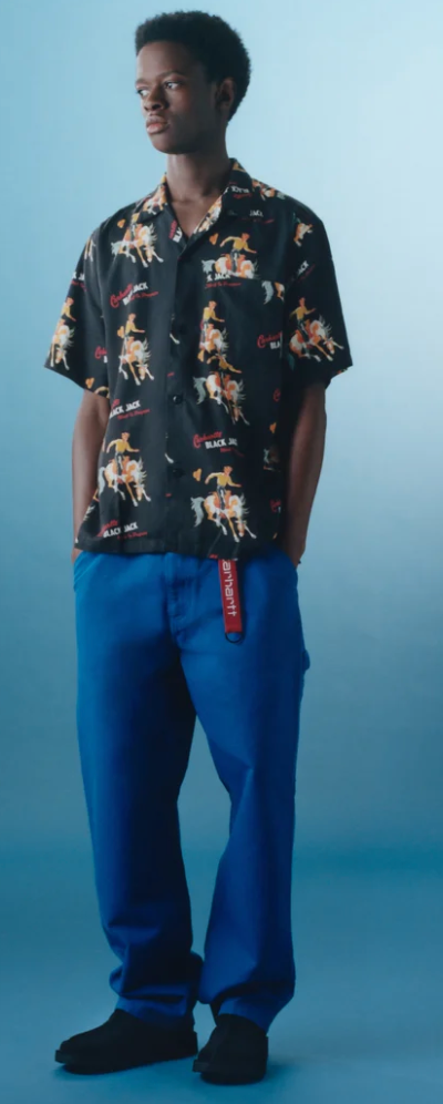 A man wearing a Carhartt WIP black graphic button-up with blue pants and branded carhartt belt