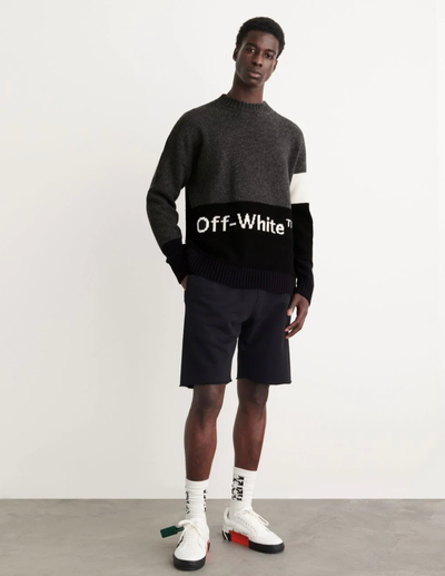 A man wearing a black Off-White sweater, black shorts and branded Off-white socks