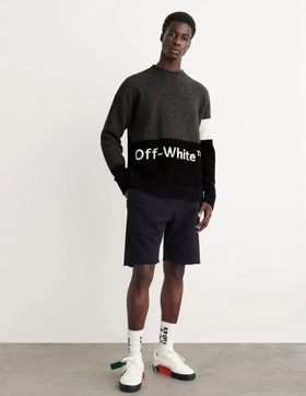 A man wearing a black Off-White sweater, black shorts and branded Off-white socks