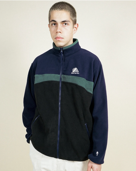 A man wearing a navy blue and green Belief fleece and white pants