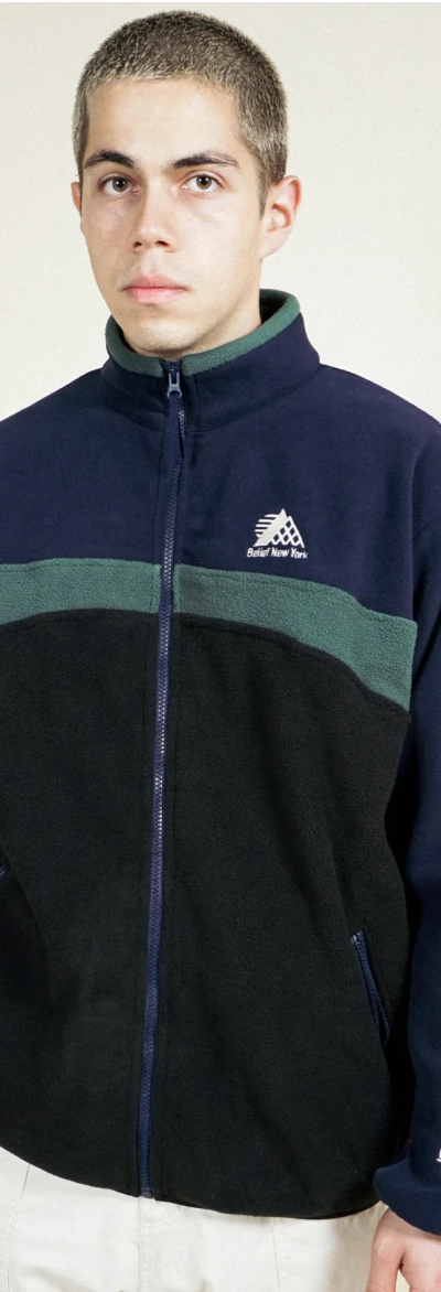 A man wearing a navy blue and green Belief fleece and white pants