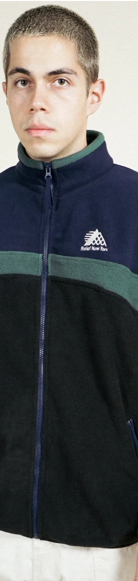 A man wearing a navy blue and green Belief fleece and white pants