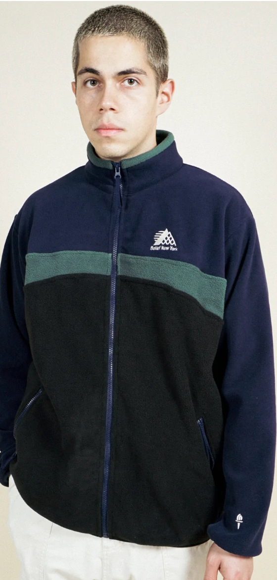 A man wearing a navy blue and green Belief fleece and white pants