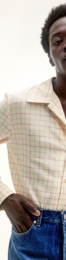 A man wearing Sefr jeans and a yellow striped long-sleeve button-up