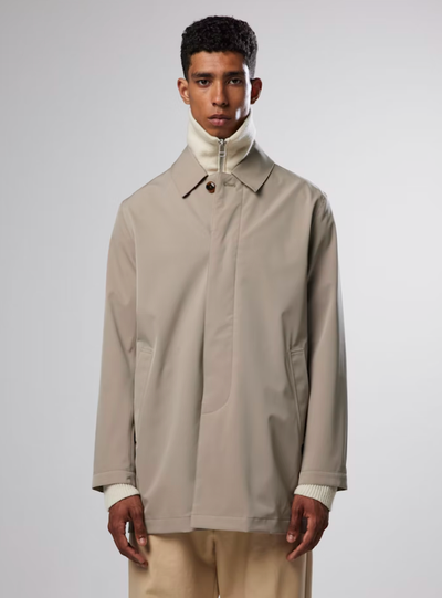 A man wearing a beige NN07 trench-coat with a beige turtle neck and brown pants