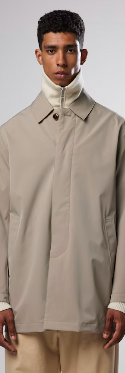 A man wearing a beige NN07 trench-coat with a beige turtle neck and brown pants