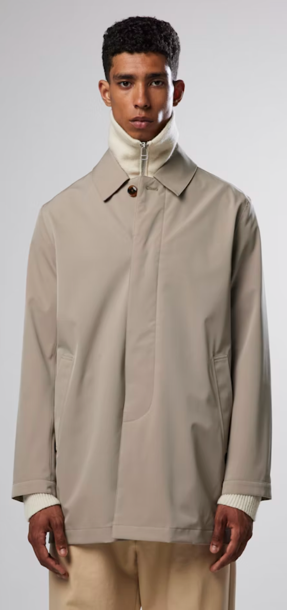 A man wearing a beige NN07 trench-coat with a beige turtle neck and brown pants