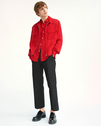 A man wearing a red Sandro button-up with a red over-jacket and black pleated pants
