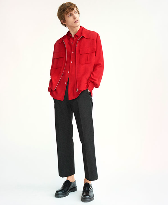 A man wearing a red Sandro button-up with a red over-jacket and black pleated pants