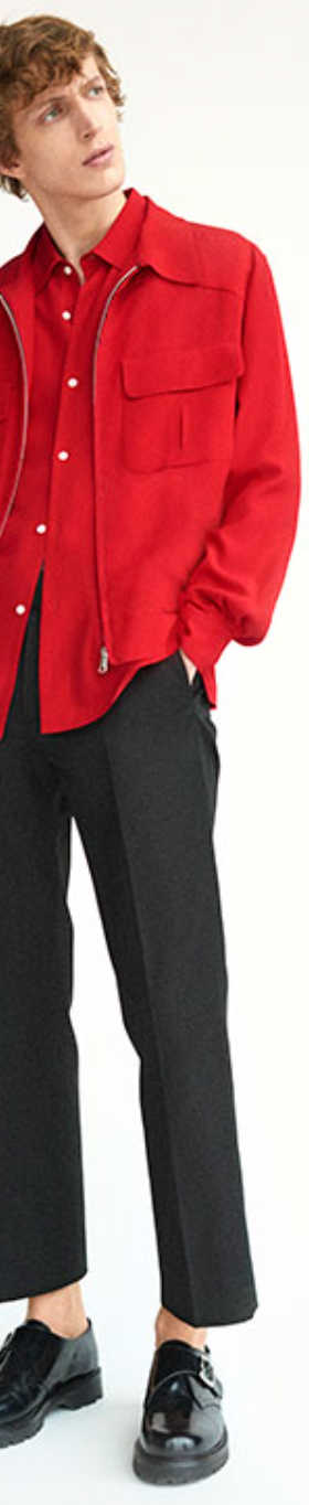 A man wearing a red Sandro button-up with a red over-jacket and black pleated pants