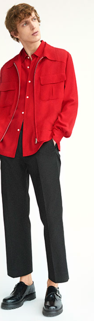 A man wearing a red Sandro button-up with a red over-jacket and black pleated pants
