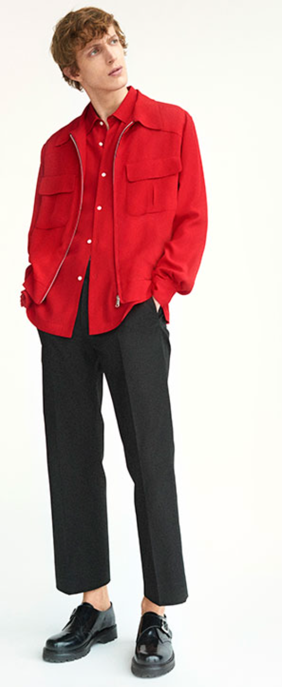 A man wearing a red Sandro button-up with a red over-jacket and black pleated pants
