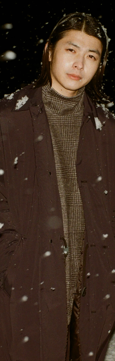 A man wearing a brown N. Hoolywood overcoat with a checkered plaid turtle neck