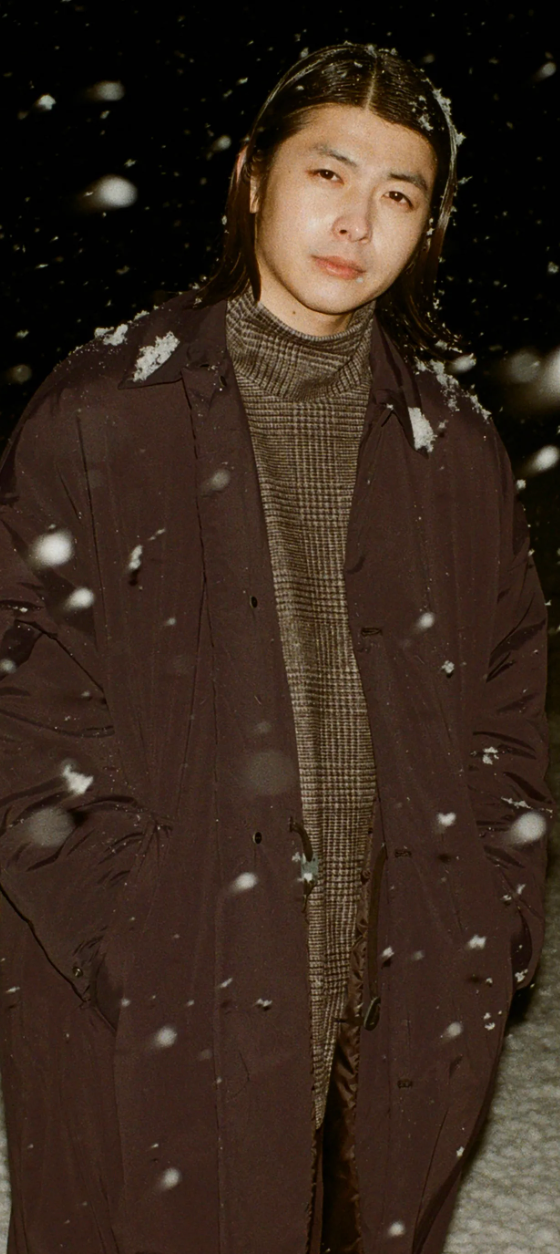 A man wearing a brown N. Hoolywood overcoat with a checkered plaid turtle neck