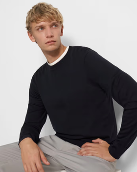 A man sitting down wearing a Theory outfit feating a navy blue sweater and grey pleated pants