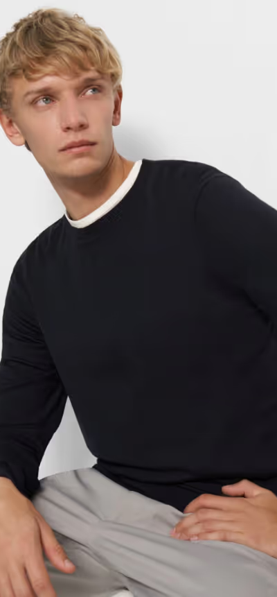A man sitting down wearing a Theory outfit feating a navy blue sweater and grey pleated pants