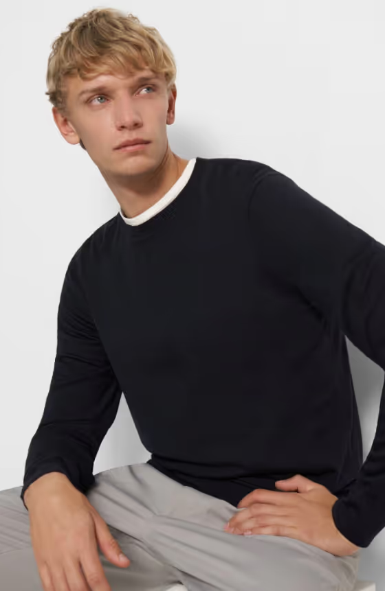 A man sitting down wearing a Theory outfit feating a navy blue sweater and grey pleated pants