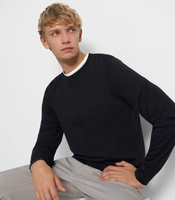 A man sitting down wearing a Theory outfit feating a navy blue sweater and grey pleated pants