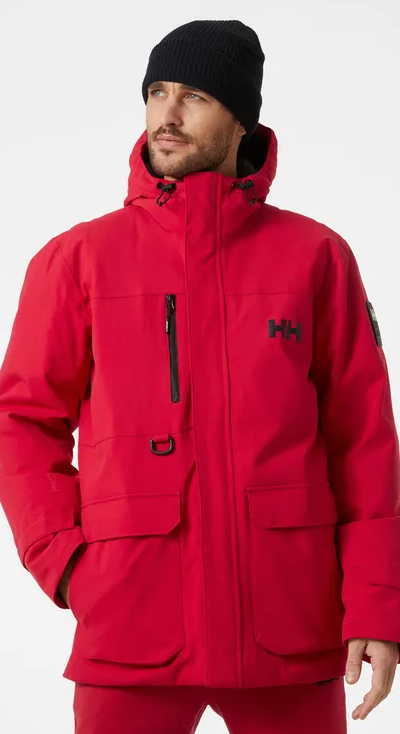 A man wearing a bright Red Helly Hanson winter Jacket with matching red pants and a black beanie