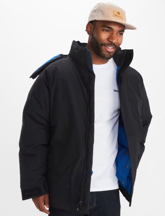 A man wearing a Marmot outfit feating a white t-shirt, black winter coat and a beige hat
