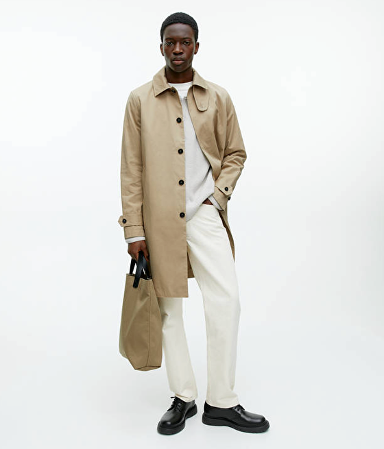 A man wearing a brown Arket trench coat and cream pants with black loafers