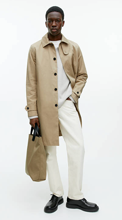 A man wearing a brown Arket trench coat and cream pants with black loafers