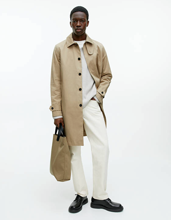 A man wearing a brown Arket trench coat and cream pants with black loafers