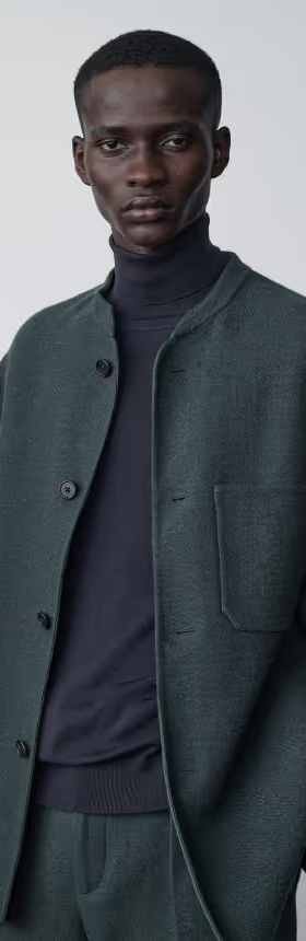 A man wearing a navy blue turtle neck with a wool green blazer by The Row
