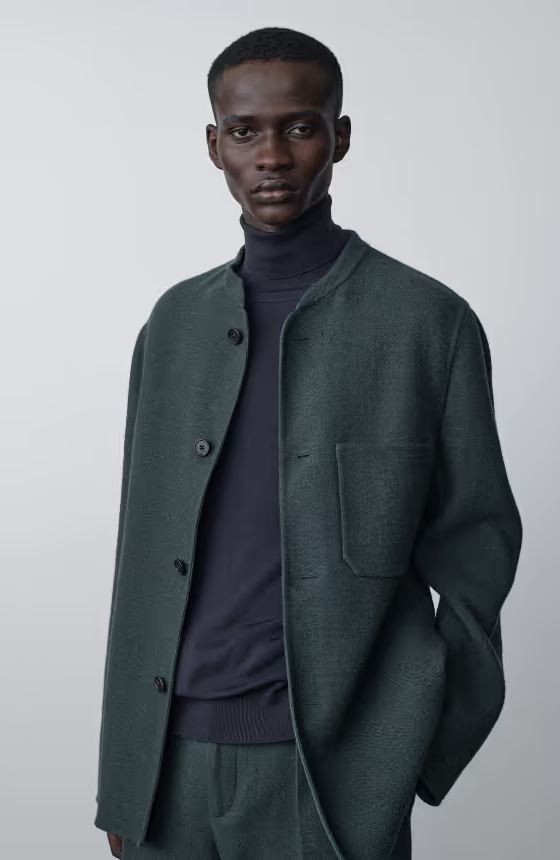 A man wearing a navy blue turtle neck with a wool green blazer by The Row