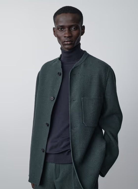 A man wearing a navy blue turtle neck with a wool green blazer by The Row